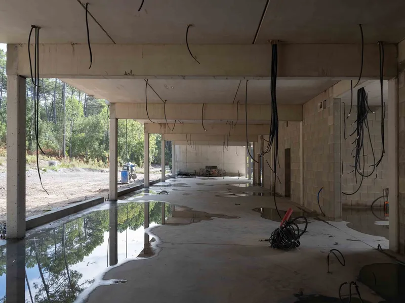 Interior view of exposed concrete columns and beams with electrical cables hanging from the ceiling