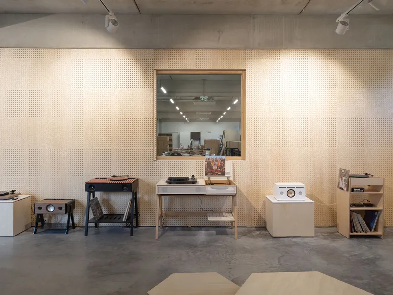 Perforated plywood wall with framed window opening into an adjacent workshop space
