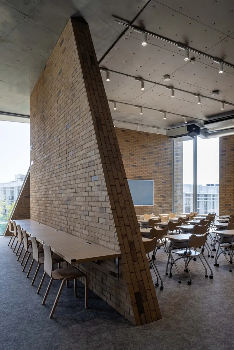Close-up of the angled brick wall partition with triangular profile beneath exposed concrete soffit with track lighting