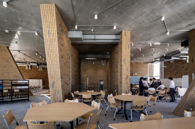 Study area with wooden tables and chairs beneath board-formed concrete ceilings and brick pilasters with students gathered