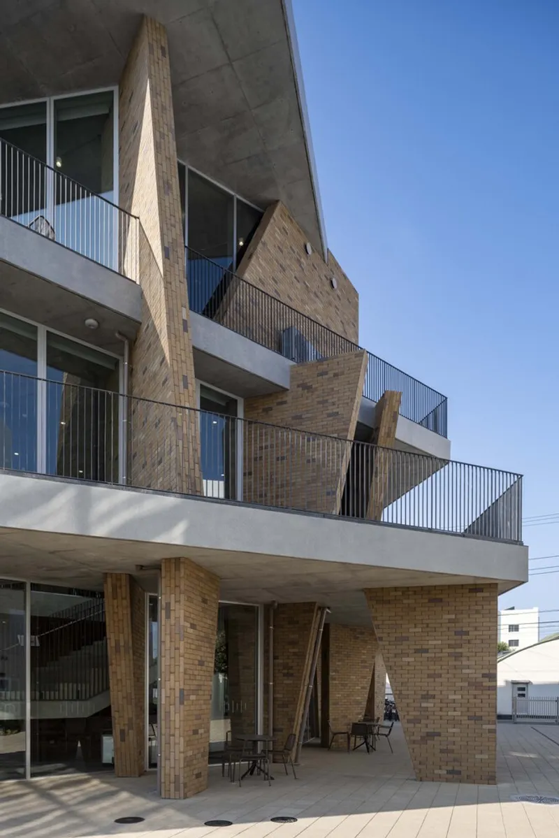 Stepped facade with cantilevered concrete slabs and angled brick walls under clear blue sky