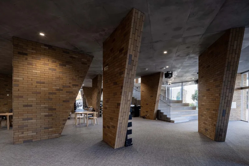 Ground floor passage with angled brick columns and exposed concrete ceiling under recessed lighting