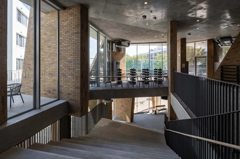 Stairwell landing with corrugated metal railings and glazed openings overlooking double height space