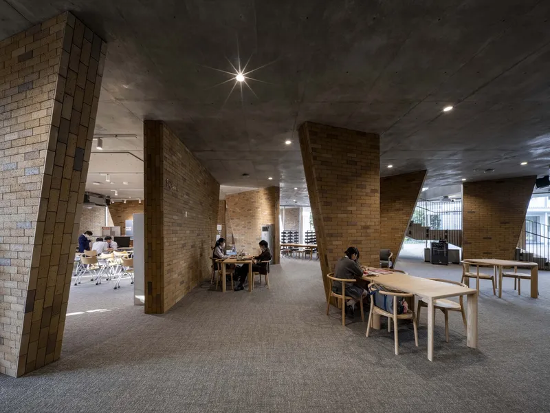 Open interior space with angled brick walls and timber furniture occupied by seated residents