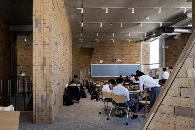 Classroom interior with variegated brick columns and exposed concrete ceiling lit by track lighting