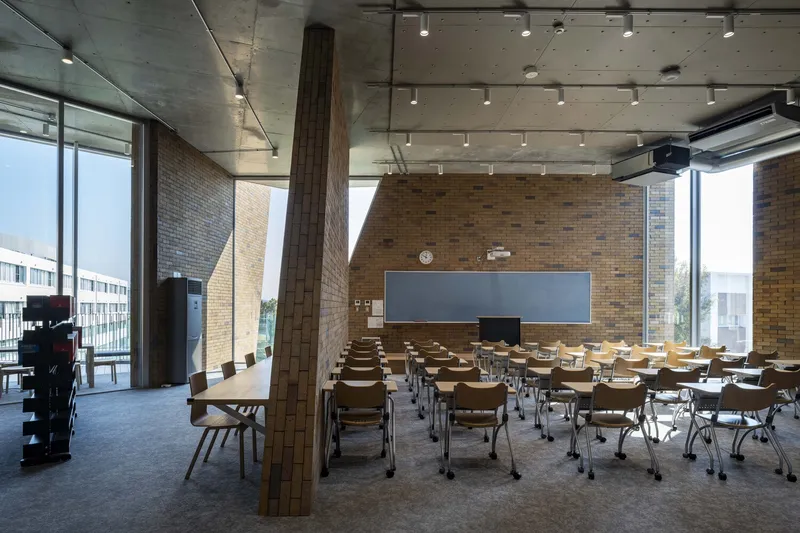 Classroom with tablet arm chairs arranged in rows beneath exposed concrete ceiling and track lighting