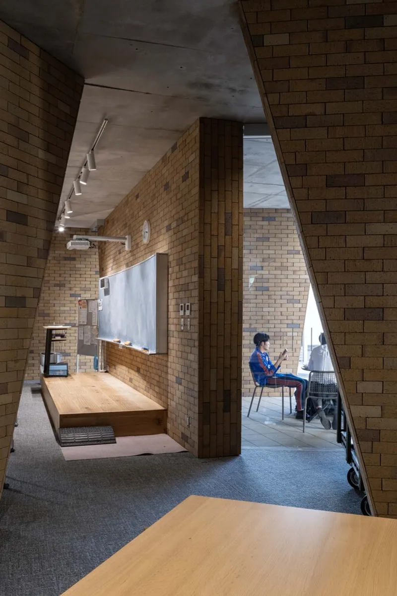 View through brick-clad interior spaces showing a student seated at a desk near the balcony railing