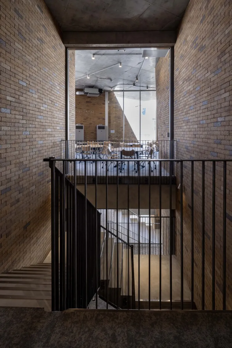 Stairwell with black metal balustrade framed by textured brick walls and exposed concrete soffits
