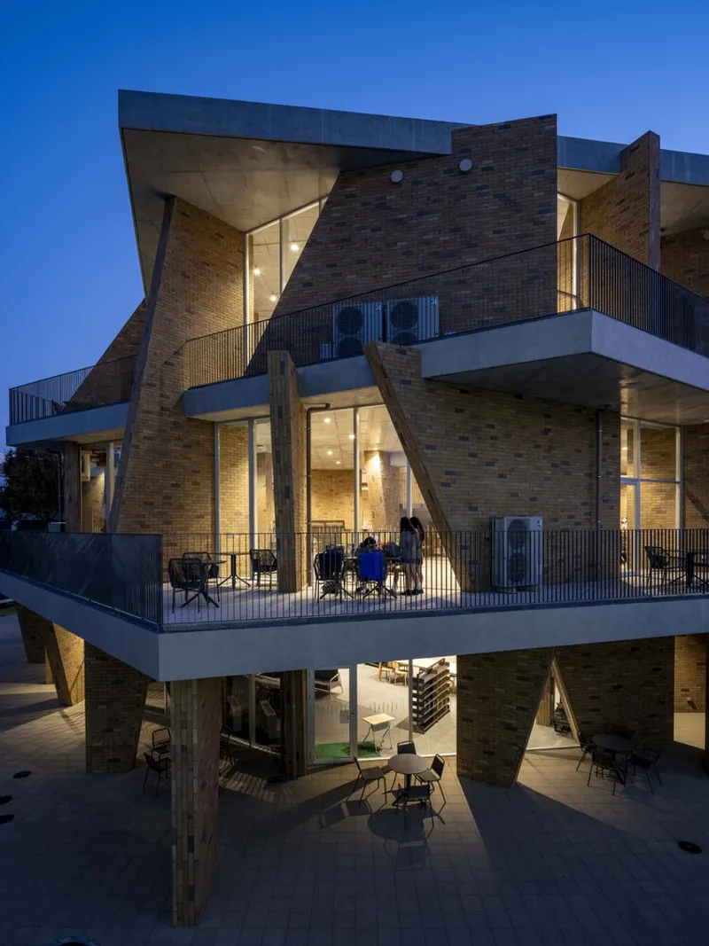 Corner view showing cantilevered balconies with timber columns and students gathering at twilight