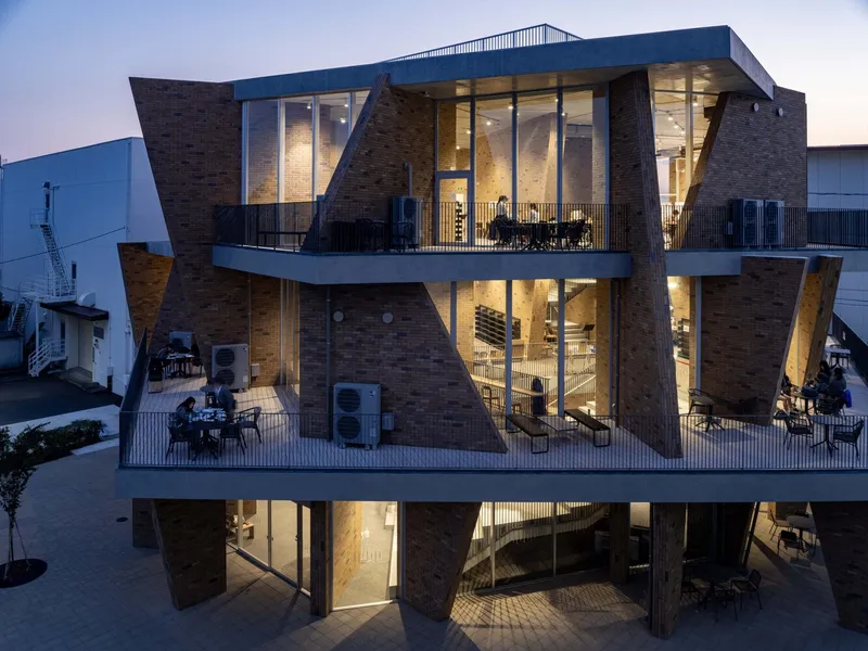 Rear elevation with stacked terraces and brick-clad pilotis supporting the upper floors at dusk