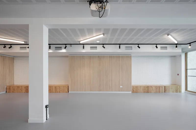 Event space: oak-slatted wall, rolling benches stored along the wall, white ceiling beams, track lighting