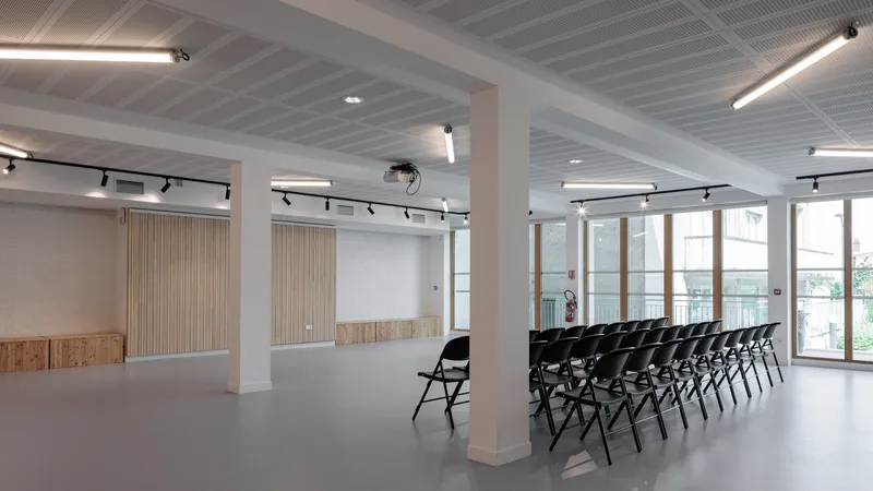 Flexible hall: column, oak wall panel, rows of black folding chairs set for an event, glass doors to terrace at far end