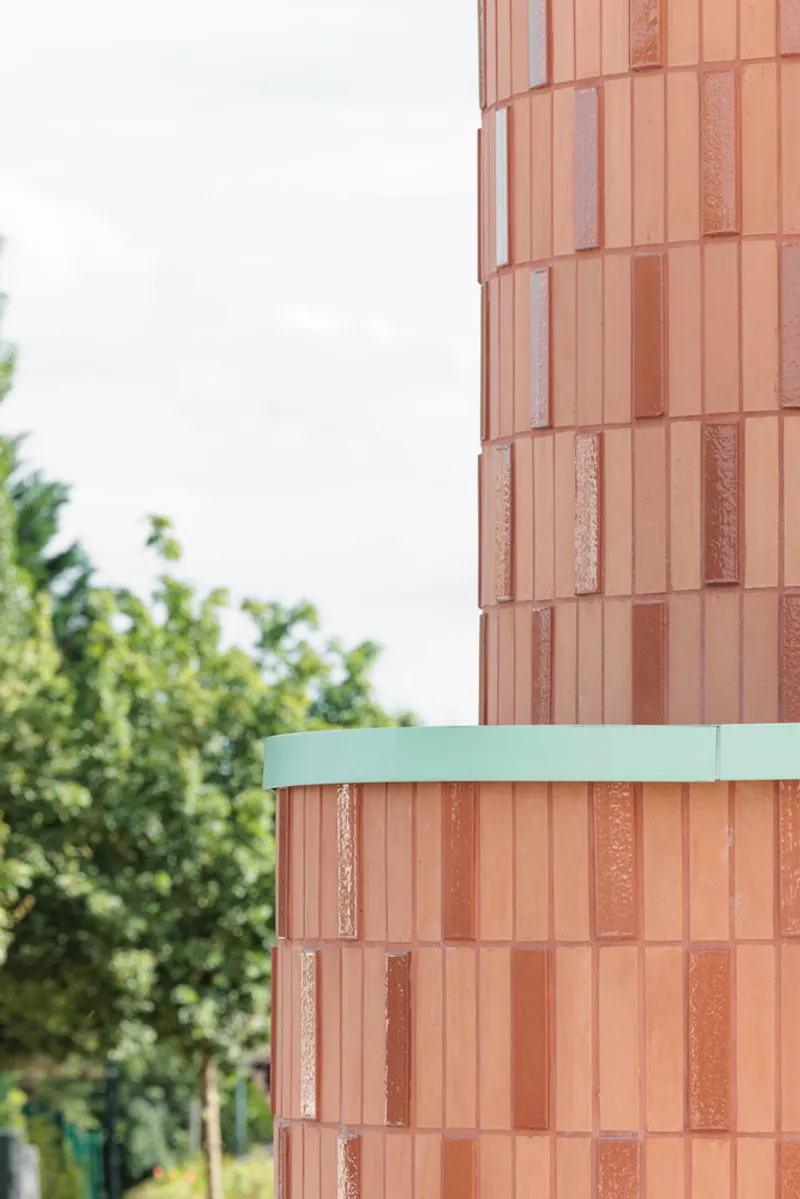 Facade detail close-up: coral terracotta tile pattern meeting the green metal railing curve