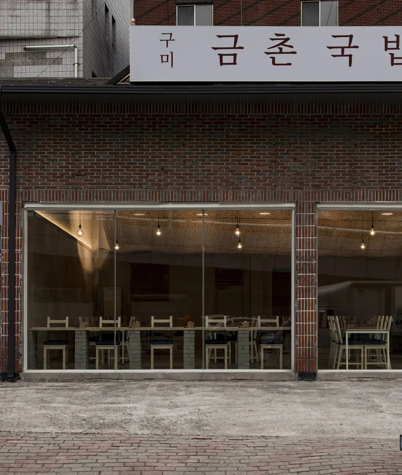 Street facade at night: dark brick, glass front, Korean signage, interior glow, counter stools visible