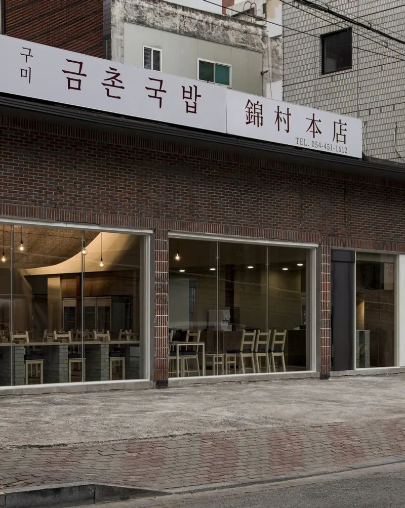 Street facade by day: dark brick storefront, full-width glass, Korean hangul signage, pavement