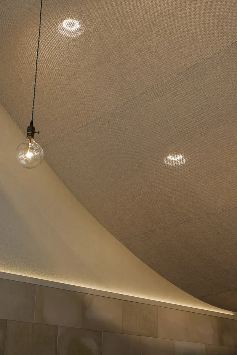 Ceiling detail: pendant bulb hanging from the lacquer paper canopy, warm glow on the textured surface