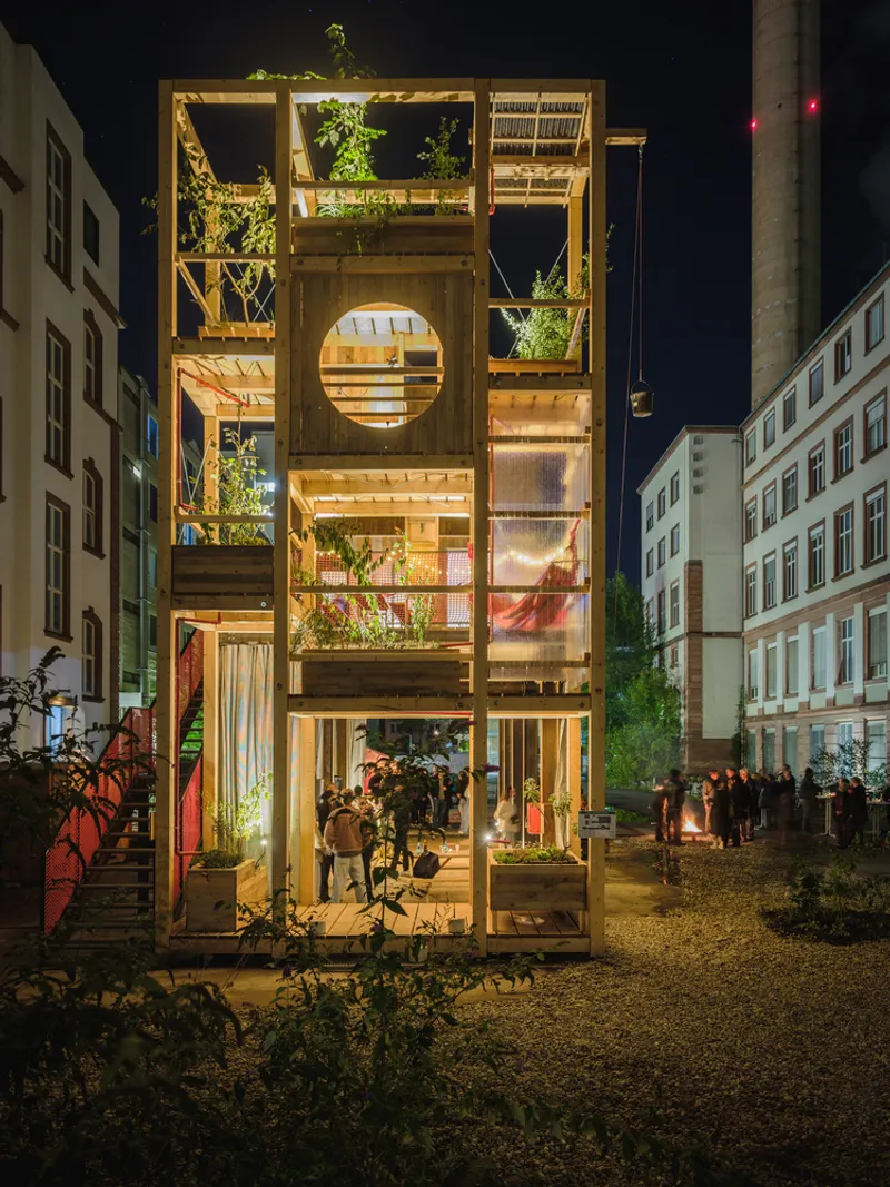 Night tower: four levels of open timber frames with plants, screens, and lights, people visible at each level
