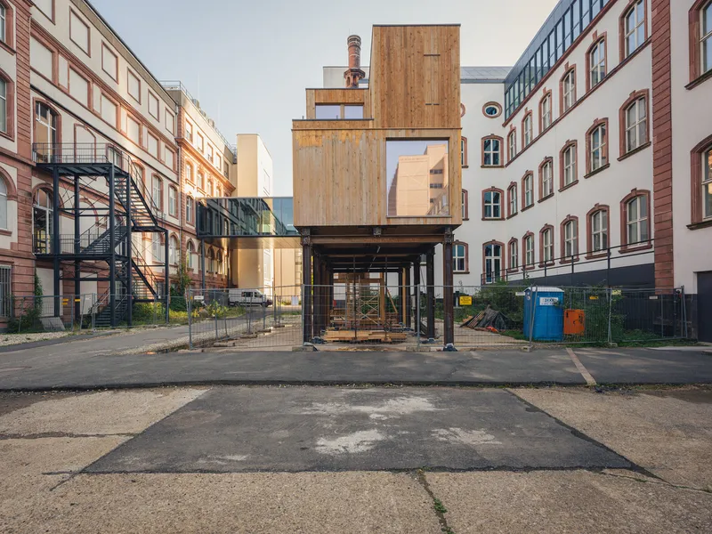 Rear view: steel and timber structure raised on steel columns, timber-clad upper modules, courtyard between historic buildings