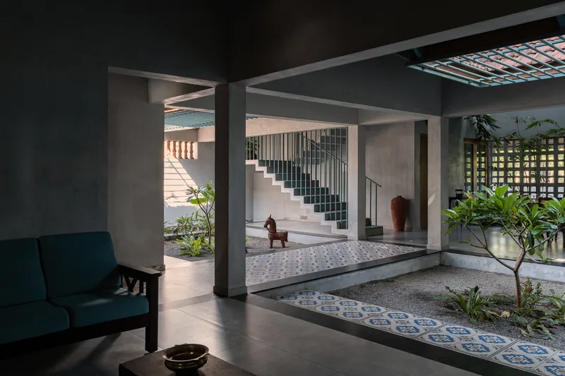 View through concrete columns into courtyard with blue patterned tile path and staircase beyond