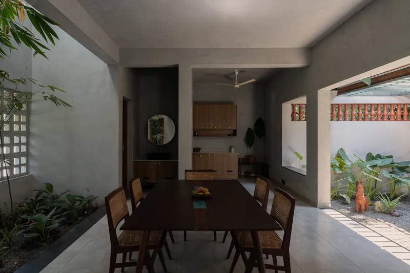 Dining table with cane chairs beneath a ceiling fan, framed by courtyard openings on both sides