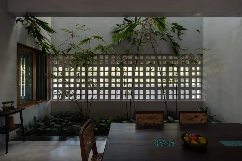 Interior wall with perforated concrete block screen behind bamboo plants and a dining table