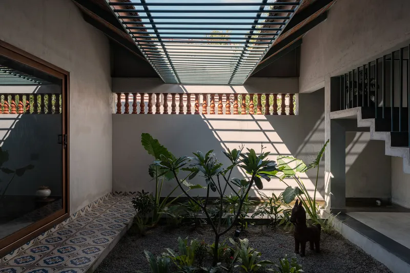 Light filtering through slatted roof onto planted courtyard with concrete stair and patterned balustrade beyond