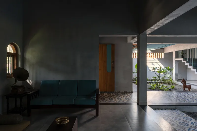 Interior living room with teal sofa opening to a planted courtyard with patterned tile flooring