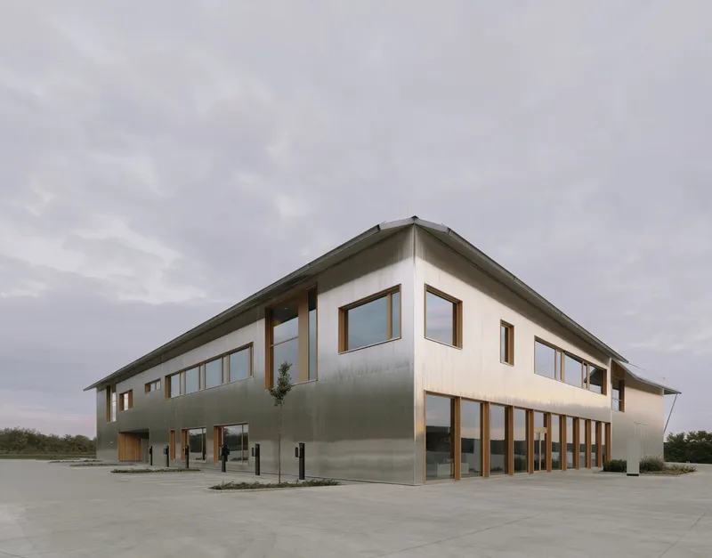 Two-story volume clad in corrugated metal with timber-framed windows under overcast sky