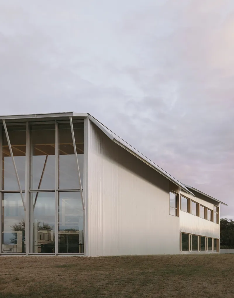 Corner facade with glass-walled entrance, diagonal bracing, and corrugated metal cladding under overcast sky