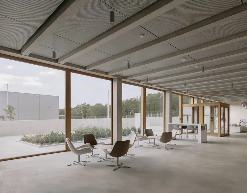 Interior lobby with timber beams, full-height glazing, lounge chairs, and view to planted courtyard