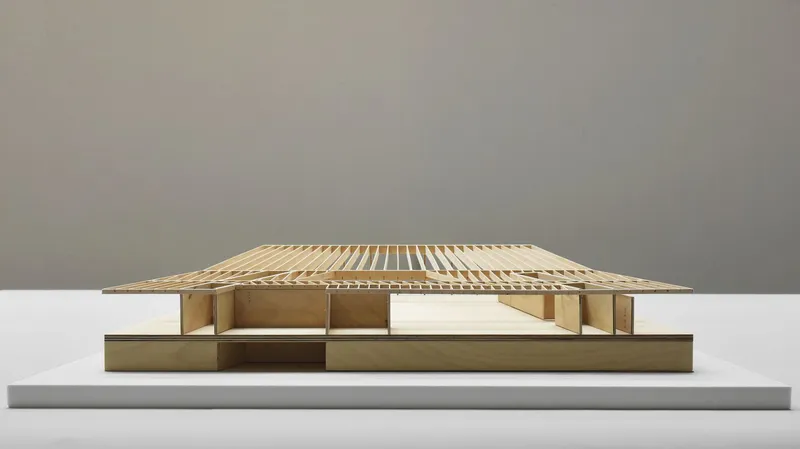 Physical model showing a low pavilion with slatted timber roof and bronze base on a neutral plinth