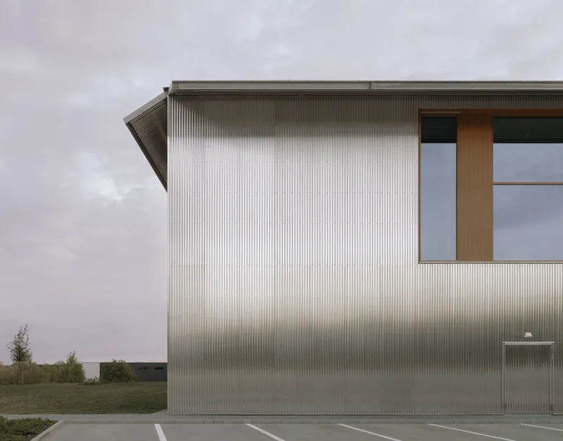 Angled facade of ribbed metal cladding with timber-framed window opening at dusk