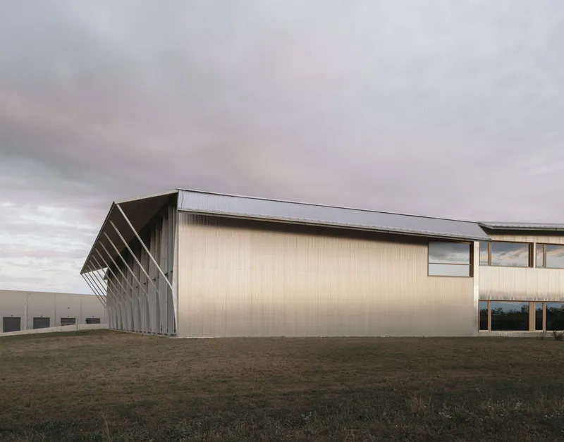 Side elevation showing the corrugated metal cladding and angled steel colonnade across open grassland