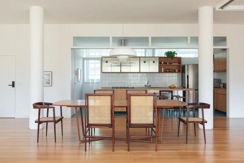 Dining and kitchen: rosewood table, cane-back chairs, white cylindrical column, stainless steel kitchen cabinets behind glass partition