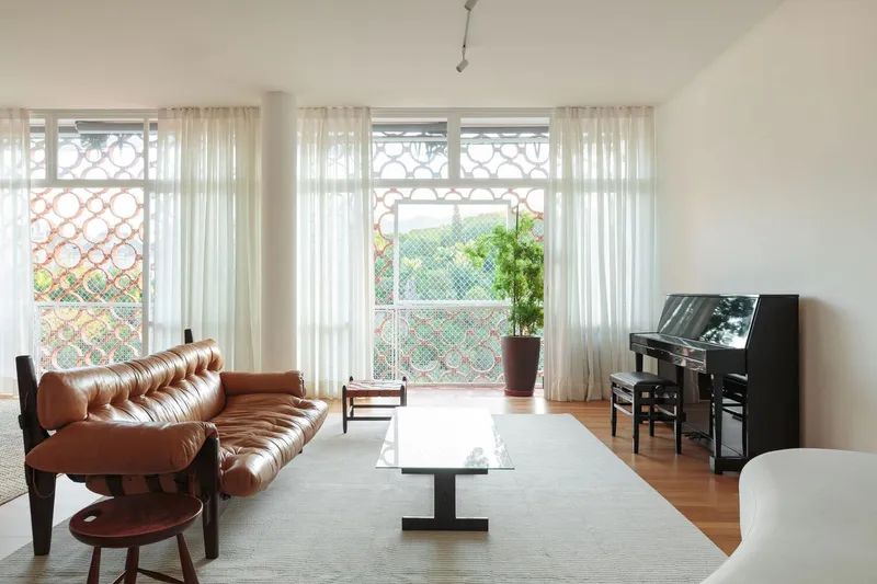 Living room: cobogó screen windows filtering light, leather Mole sofa, rosewood chair, piano, sheer curtains, parquet floor