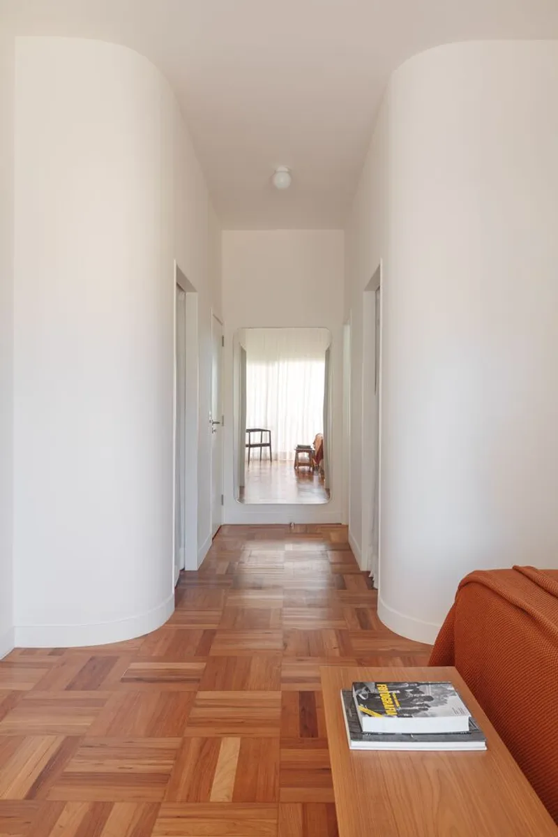 Corridor: parquet flooring in basket-weave pattern, white curved walls, globe light, leather sofa edge, magazine on timber table
