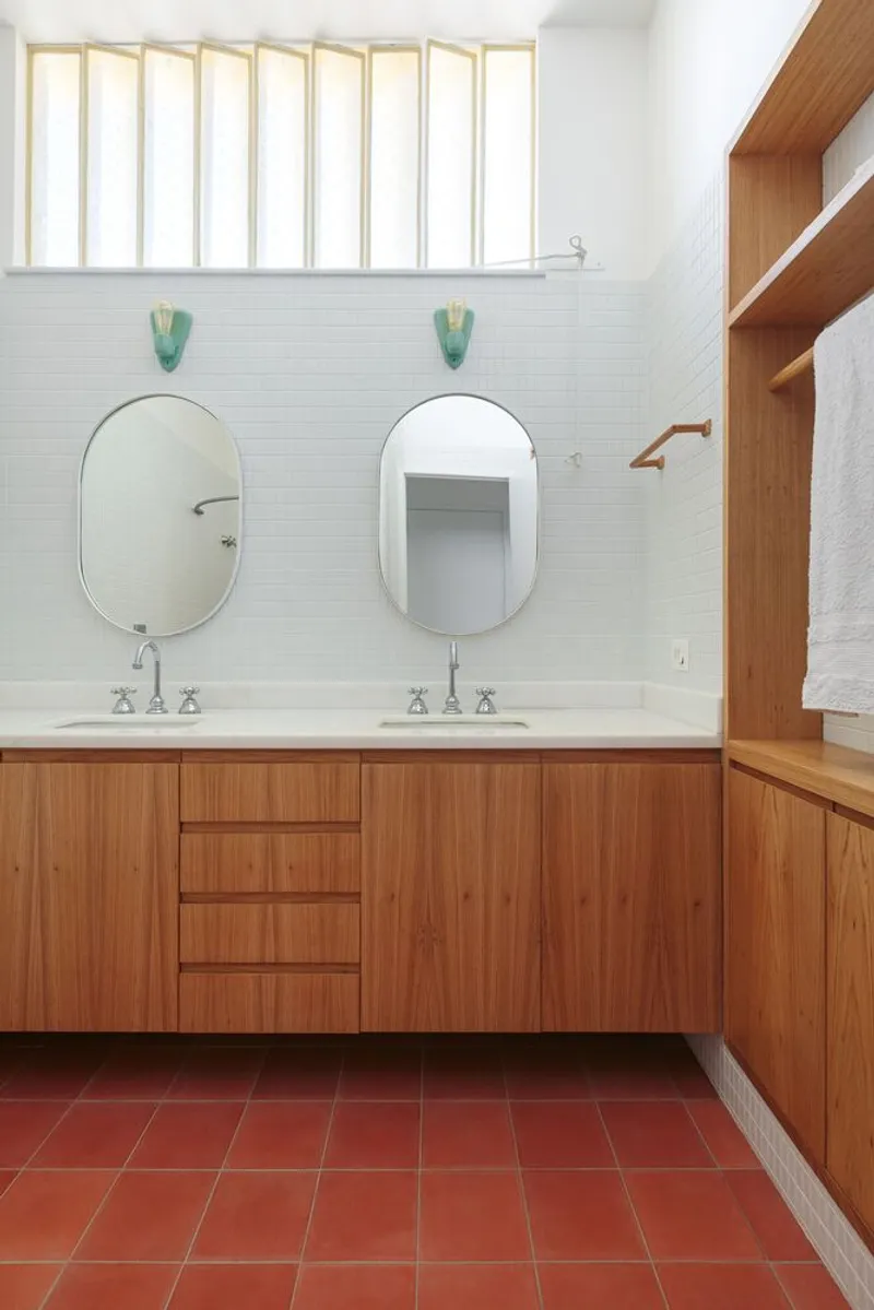 Main bathroom: double vanity with oak cabinets, white tile, oval mirrors, terracotta floor tiles, louvre window above