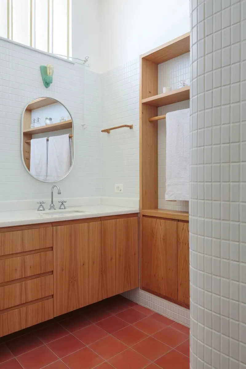 Bathroom detail: oak vanity, white tile walls, oval mirror, towel shelf, louvre window letting in light