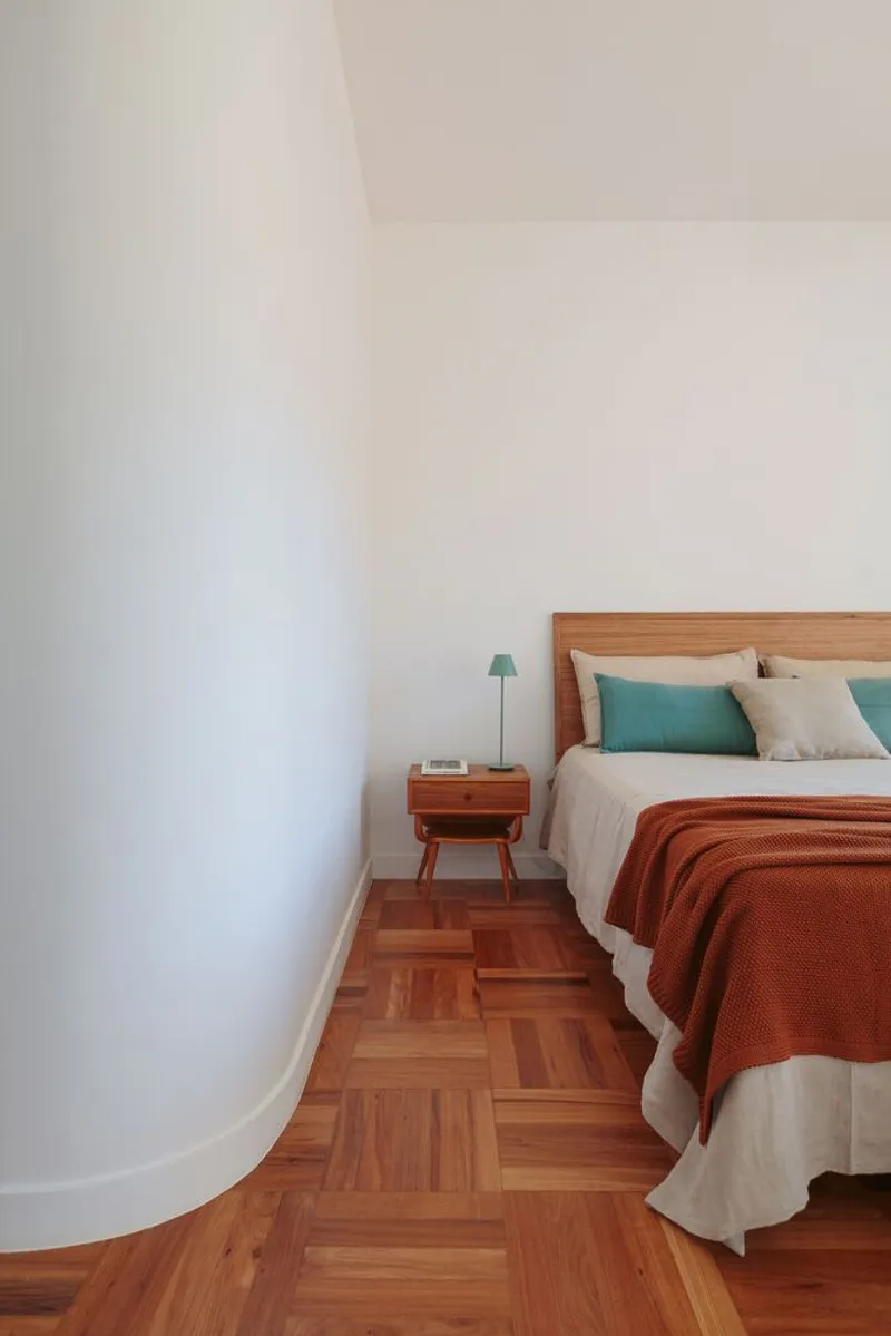 Bedroom: curved white column meeting the wall, oak headboard, terracotta throw, teal cushions, parquet floor, timber nightstand