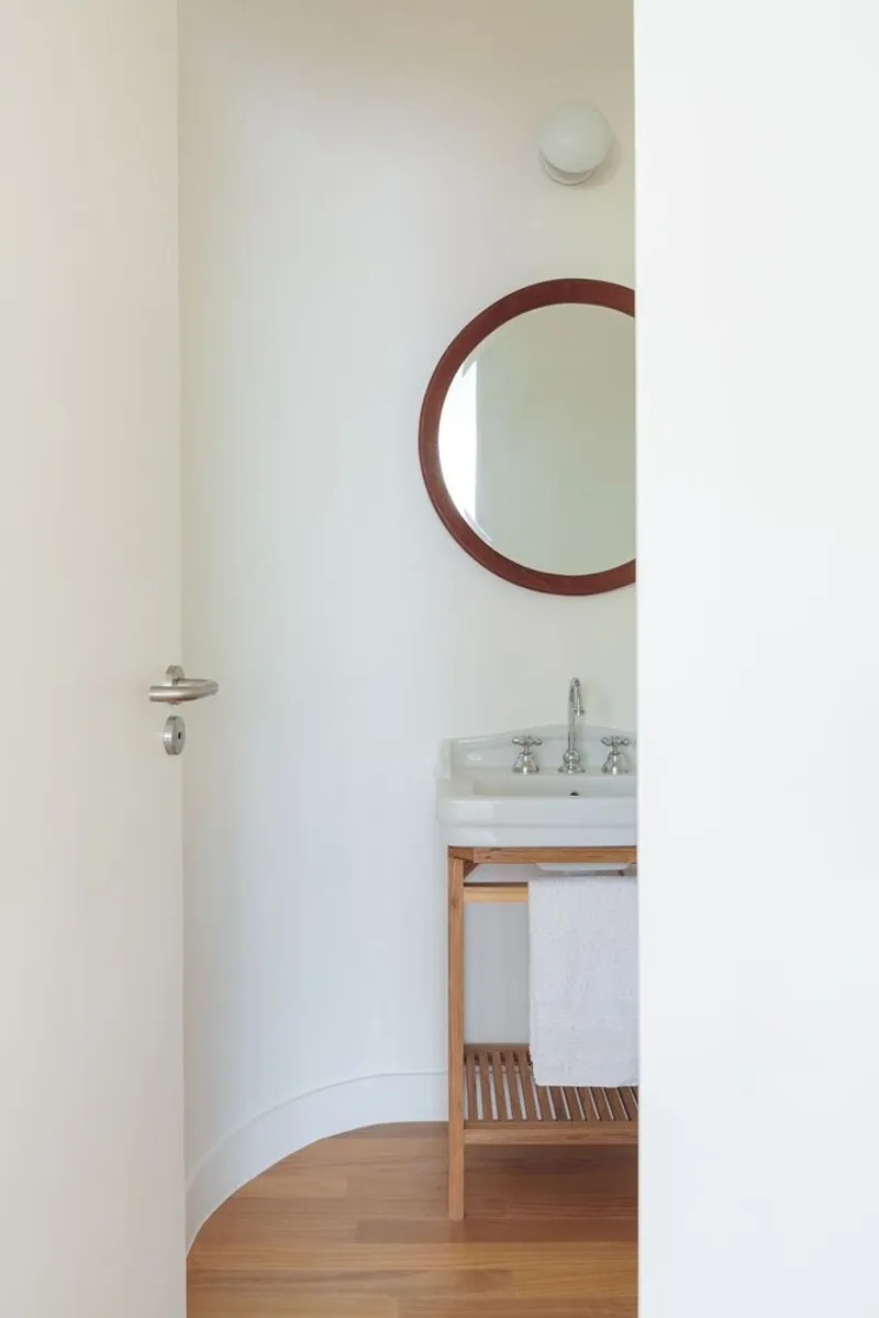 Powder room: round timber mirror, pedestal basin on oak shelf, curved wall, globe light, oak floor