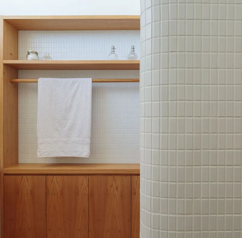Towel shelf detail: oak frame, white tile, towel rail, curved tiled column at right edge