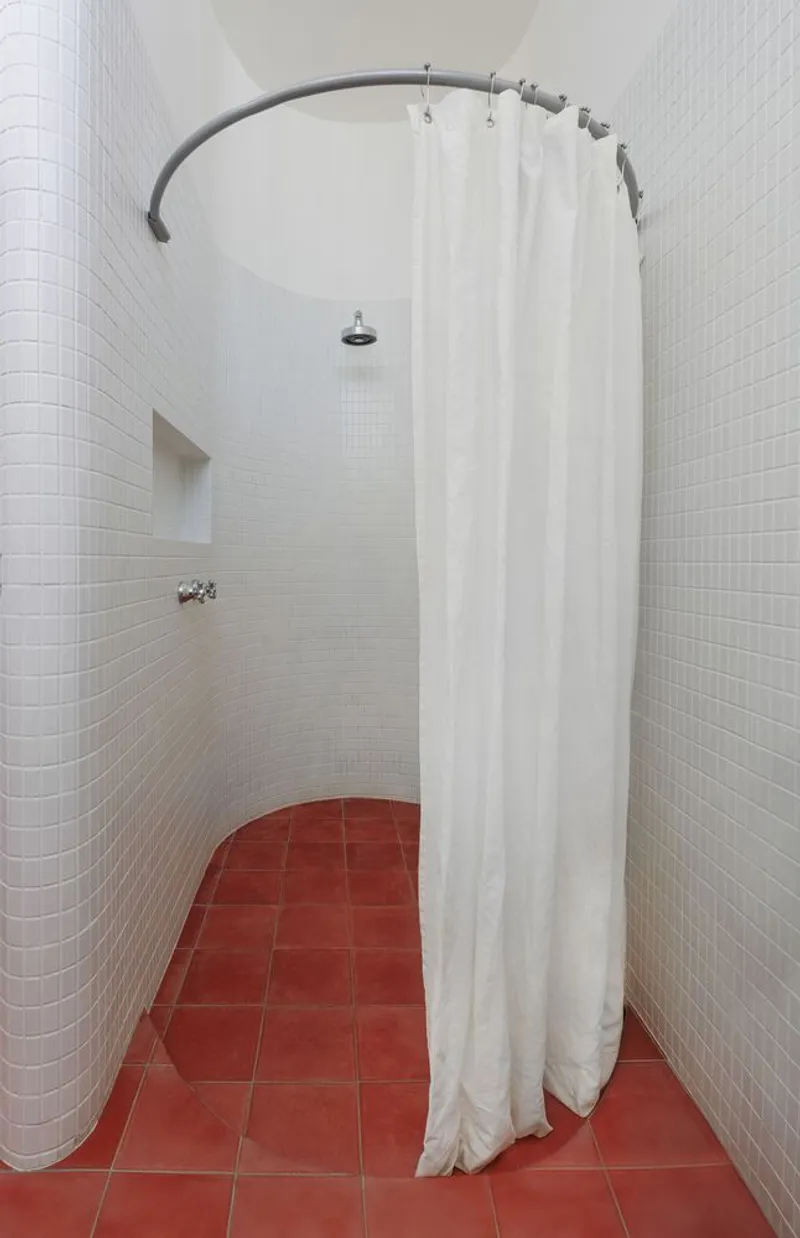 Shower: curved curtain rail, white curtain, terracotta floor tiles, white tile walls