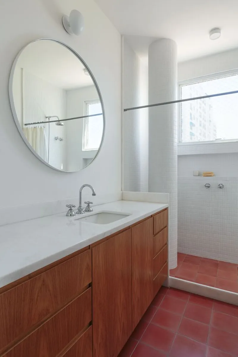 Bathroom: oak vanity, round mirror, terracotta floor, white tile, shower area beyond