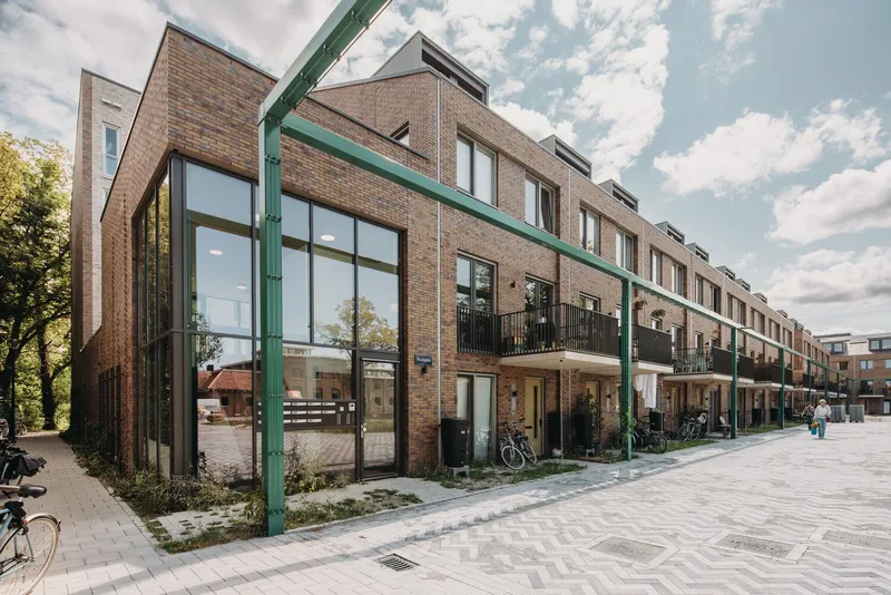 Street view of the brick row house facade with green steel columns and balconies under cloudy skies