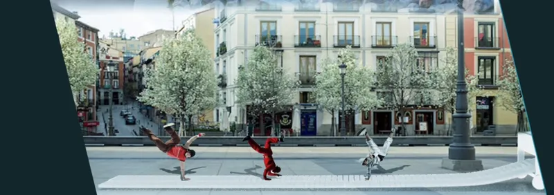 Street-level view of three performers breakdancing on a white folded platform in a plaza with trees