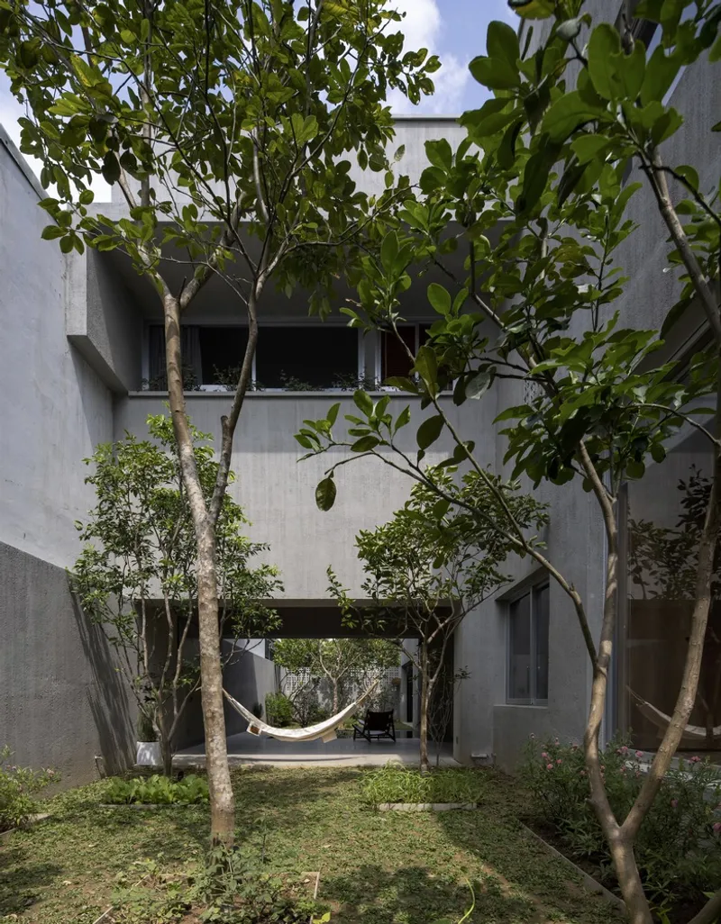 Garden courtyard with trees and planted lawn between concrete volumes under open sky