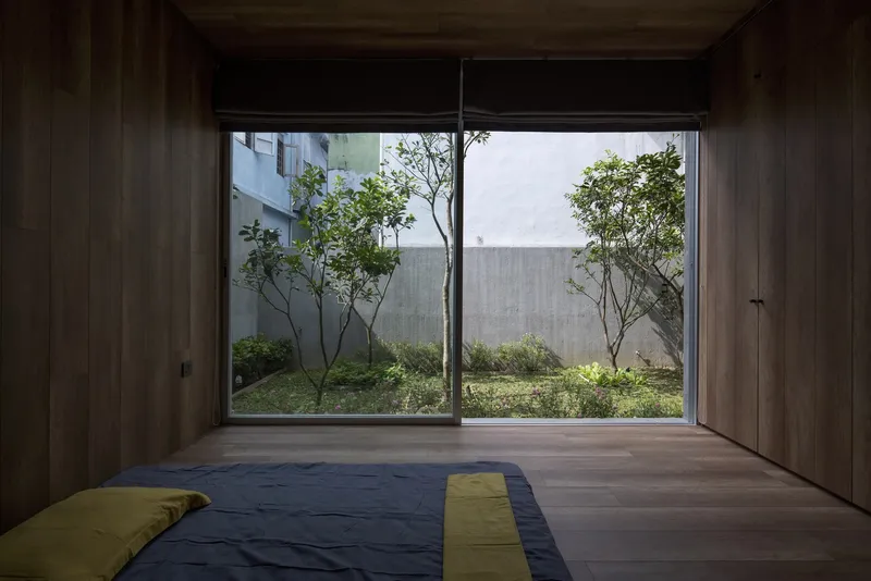 Timber-lined bedroom with floor mattress overlooking a planted courtyard through sliding glass doors