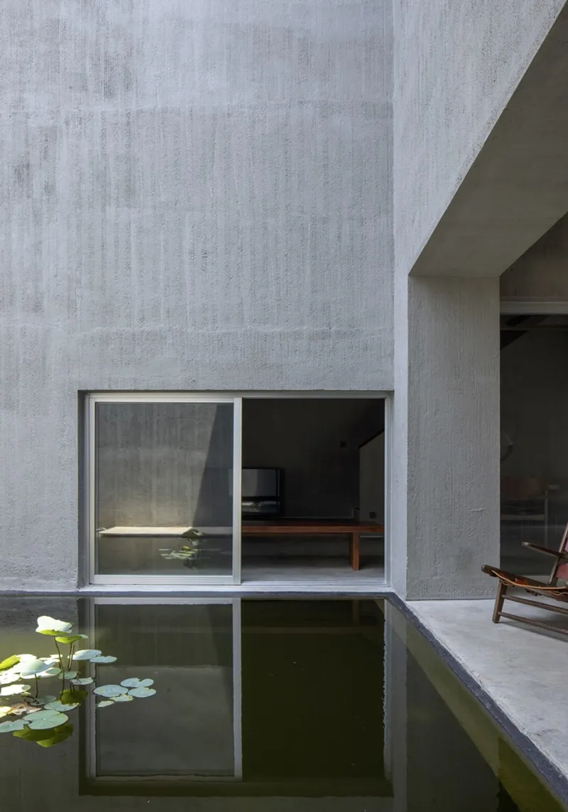 Concrete wall with sliding glass doors reflected in a pond bordered by lily pads
