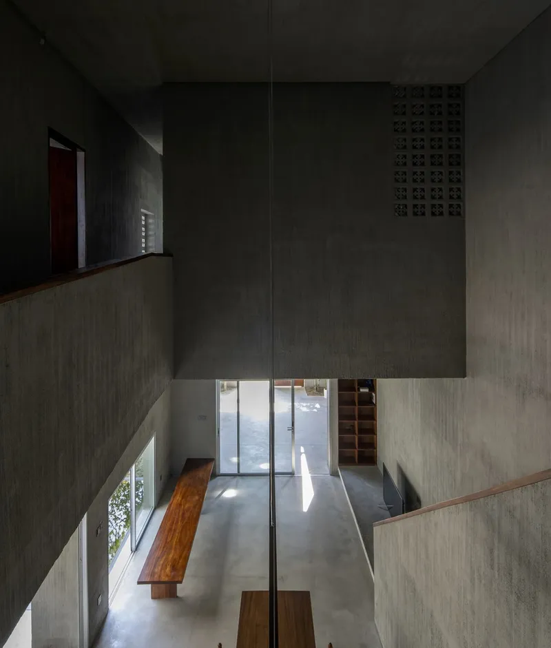 Double-height void with board-formed concrete walls and timber benches on polished concrete floor lit by daylight
