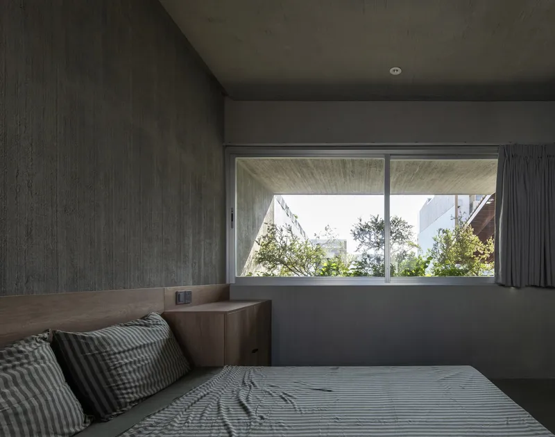 Bedroom with platform bed and horizontal window overlooking garden vegetation in daylight